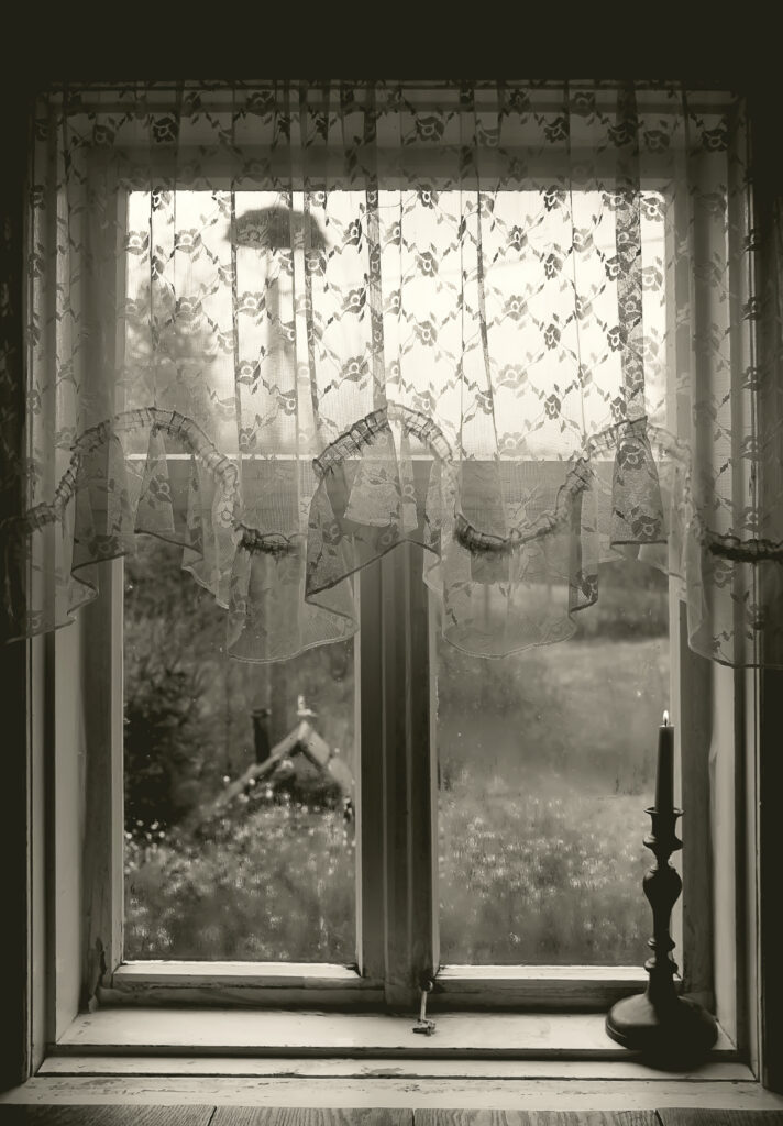 A grainy black-and-white photograph shows a window with a candle in the foreground.